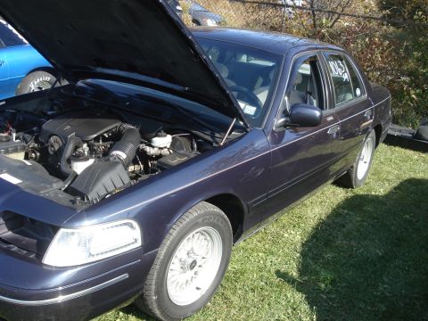 2000 Ford Crown Victoria - A dark blue 2000 Ford Crown Victoria sedan is parked on grass with its hood open, revealing the engine bay.