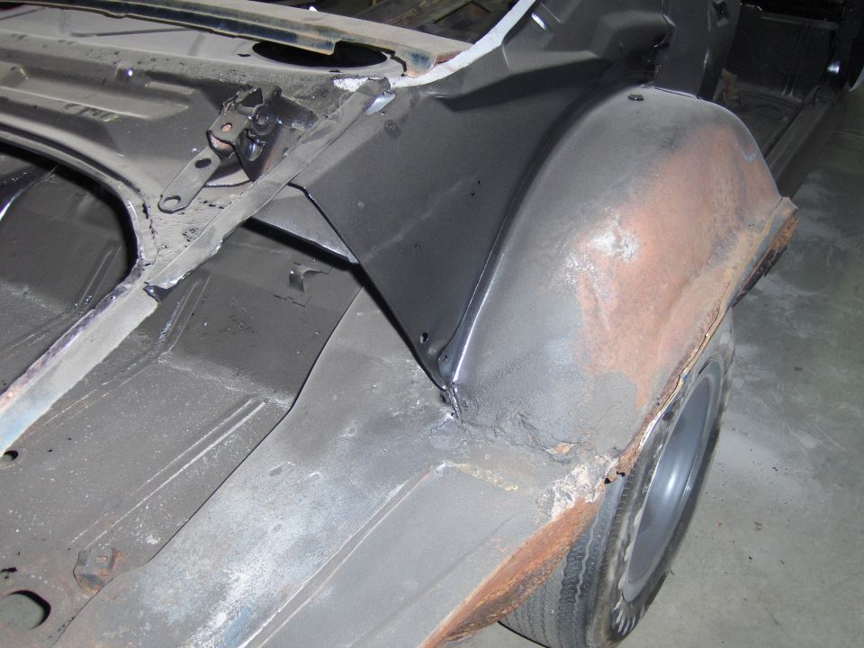 close-up of rusty rear wheel well and frame of a car undergoing restoration