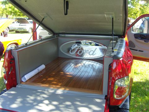 2007 Ford Mustang - The custom bed of a red Ford pickup truck features a polished wood floor and a prominent Ford oval logo.