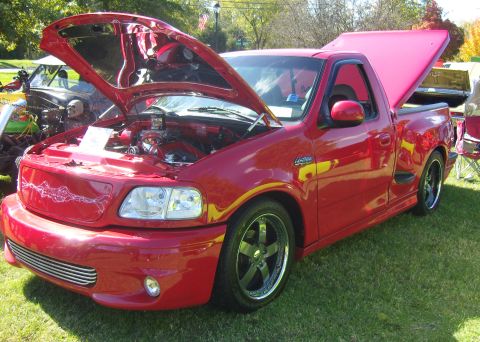 2007 Ford Mustang - A red pickup truck is displayed with its hood and bed open, parked on grass at an outdoor event.