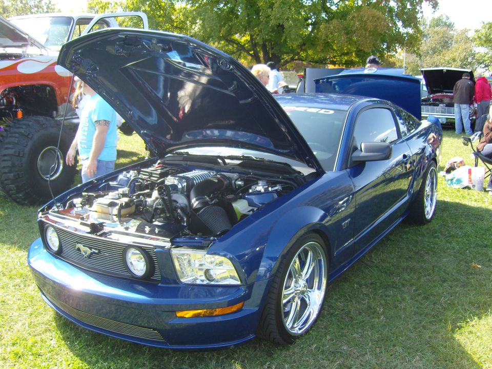 Blue Ford Mustang with hood open, showing engine and chrome wheels