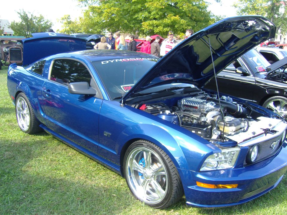 Blue 2007 Ford Mustang GT with hood open, displaying a supercharger. Another car is visible to the right