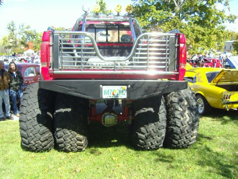 2007 Ford Mustang - A heavily modified truck with massive tires is parked on grass next to a vintage yellow car.
