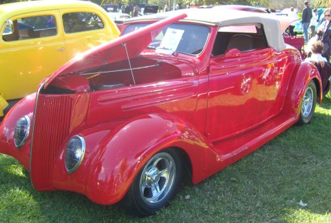 2007 Ford Mustang - A red convertible hot rod is displayed with its hood open, parked on grass next to a yellow sedan.