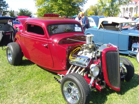 2007 Ford Mustang - A custom red hot rod with a prominent V8 engine is displayed outdoors, with other vehicles visible in the background.
