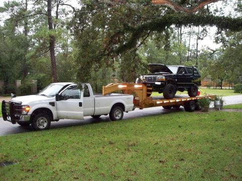 1995 Ford Bronco - A 1995 Ford Bronco is loaded onto a trailer and towed by a white pickup truck.