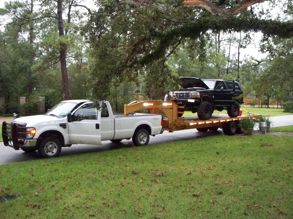 1995 Ford Bronco on a trailer, hood open, towed by a white pickup truck
