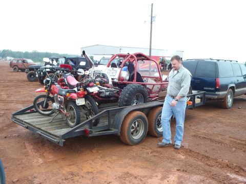 1995 Ford Bronco - A man stands by a trailer loaded with motorcycles and a buggy, with a blue Chevrolet Suburban parked behind it.