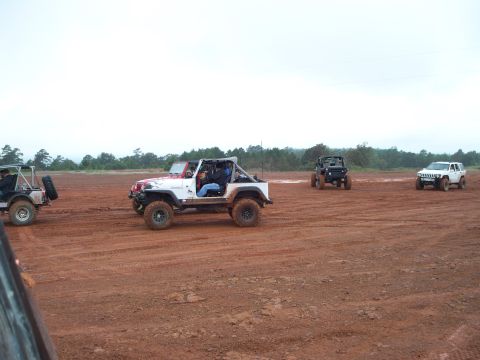 1995 Ford Bronco - Multiple off-road vehicles are seen navigating a dirt track under an overcast sky.
