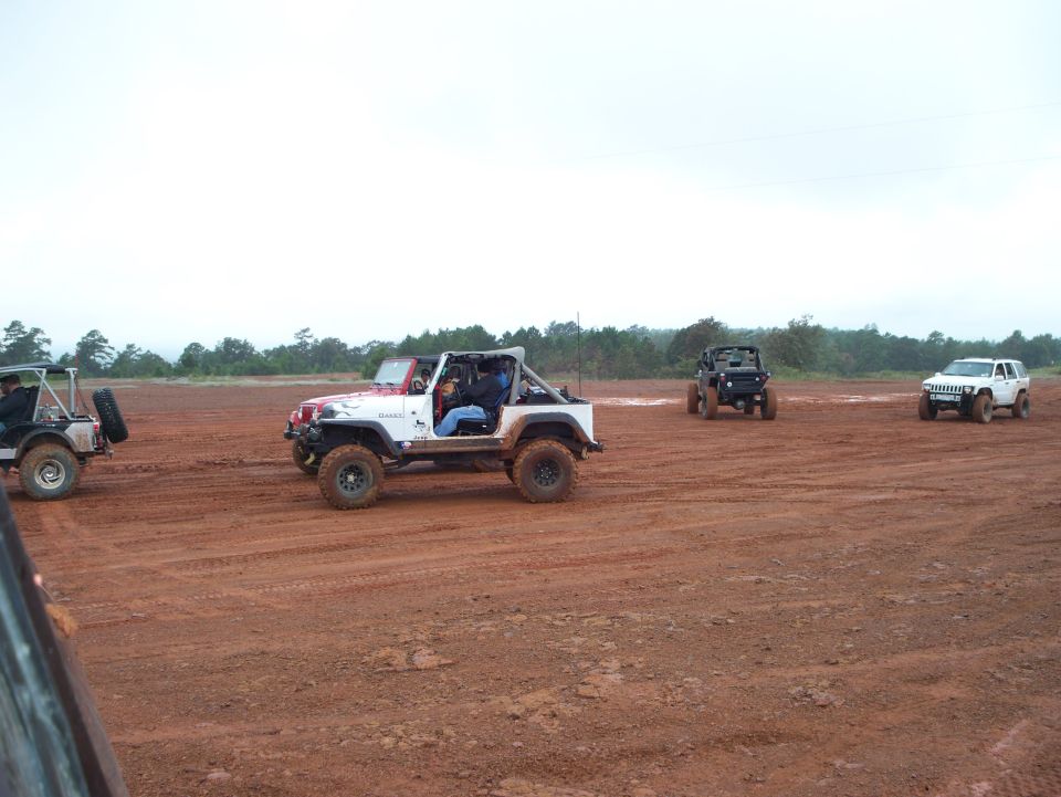 Several off-road vehicles driving on a dirt track with trees in the background