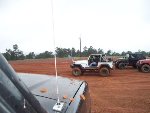 1995 Ford Bronco - Multiple off-road vehicles are gathered on a dirt track under an overcast sky.