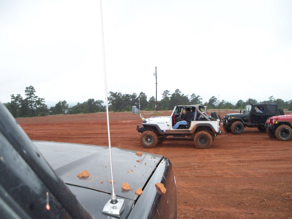 Several Jeeps parked on a muddy dirt track with trees in the background