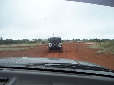 1995 Ford Bronco - A convoy of off-road vehicles, including a white Jeep Wrangler, navigates a muddy dirt track under an overcast sky.