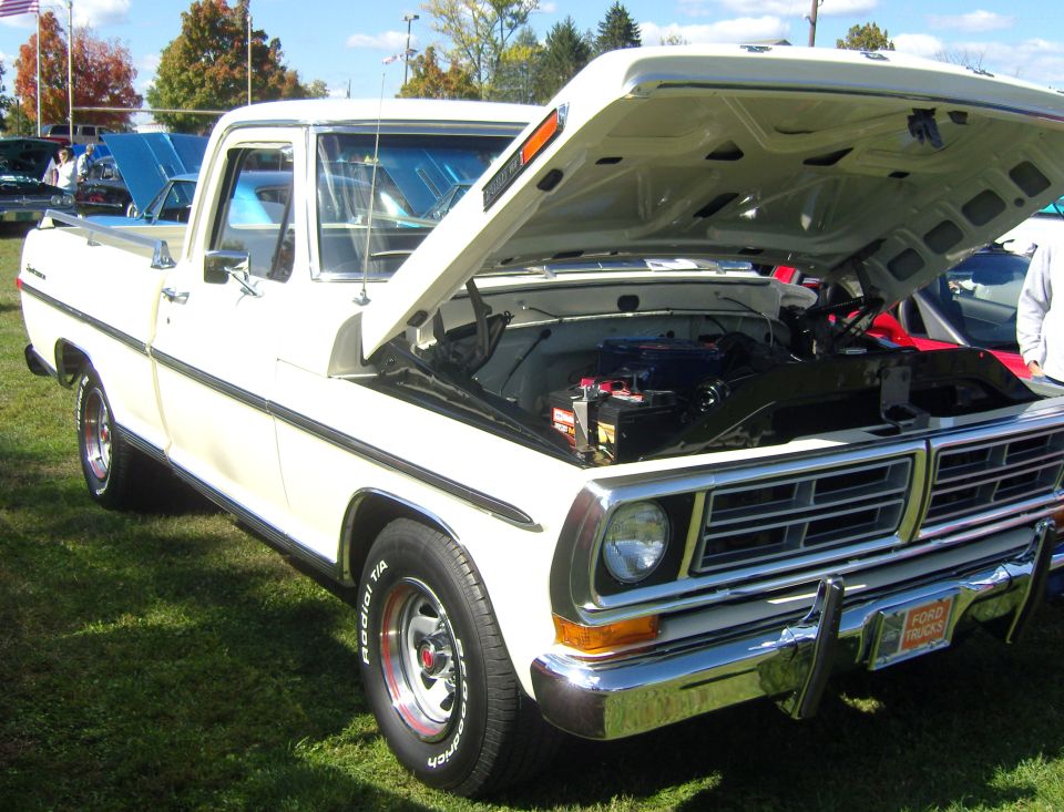 White Ford pickup truck, hood open, showing engine bay. Grille indicates 1970s model