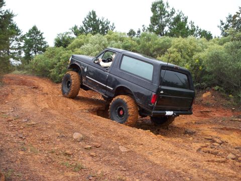 1995 Ford Bronco - A black Ford Bronco navigates a challenging off-road trail with steep inclines and muddy terrain.