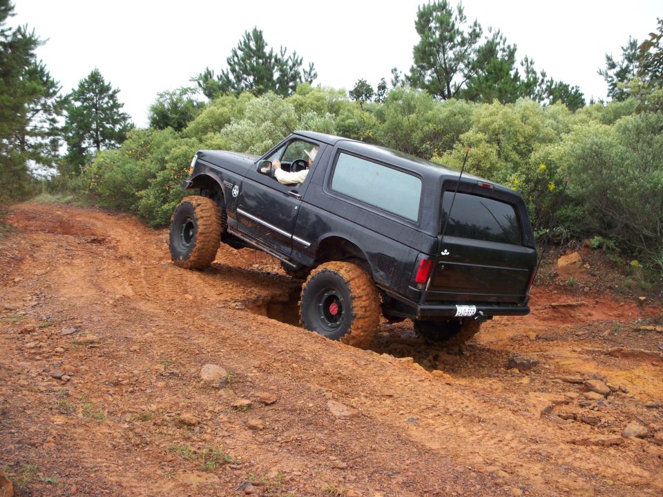 Black 1992 Ford Bronco with lifted suspension and large tires navigating a muddy ditch on a dirt trail