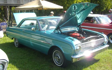 2007 Ford Mustang - A teal 1963 Ford Falcon coupe is displayed with its hood open, revealing the engine, at an outdoor car show.