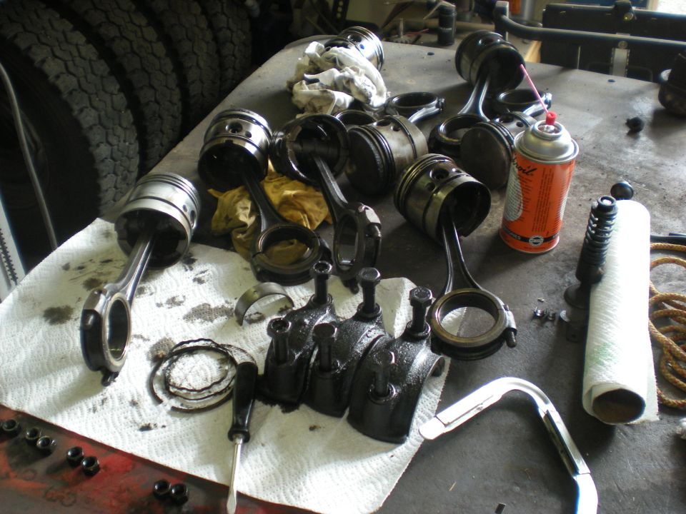 Engine pistons and connecting rods disassembled on a workbench with a can of spray and a roll of paper towels
