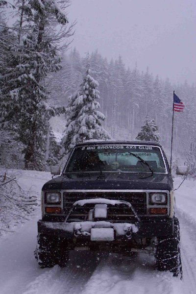 1982 Ford Bronco - Ford Bronco navigates a snowy forest road, flying an American flag.