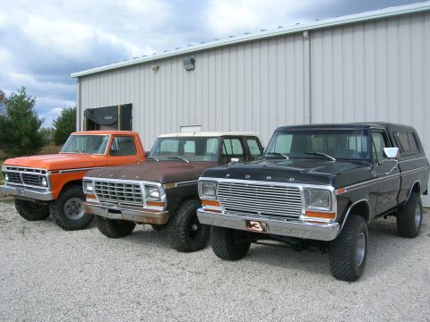 1975 Ford F-250 - Three Ford trucks, including a black 1975 F-250 with a camper shell, are lined up outside a building.