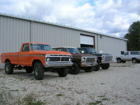 1975 Ford F-250 - Several Ford trucks and Broncos are lined up in front of a metal building on a cloudy day.