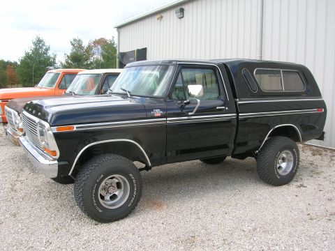 1975 Ford F-250 - A black 1975 Ford F-250 pickup truck, identified as a 'Highboy', is parked in front of a building alongside other trucks.