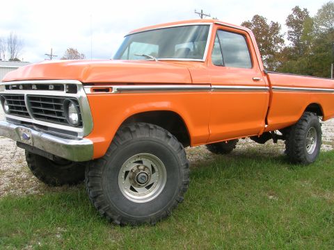 1975 Ford F-250 - An orange 1970s Ford pickup truck shown from a 3/4 front angle, lifted with large mud-terrain tires on chrome/aluminum wheels and a chrome…