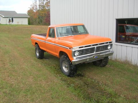 1975 Ford F-250 - This orange Ford F-250 pickup truck is parked on a grassy area next to a building with a large window.