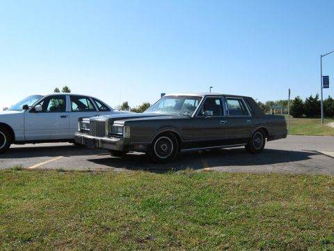 2000 Mercury Grand Marquis - Two sedans are parked in a lot under a clear blue sky.
