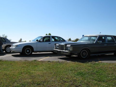 2000 Mercury Grand Marquis - Two sedans are parked in a lot under a clear blue sky.