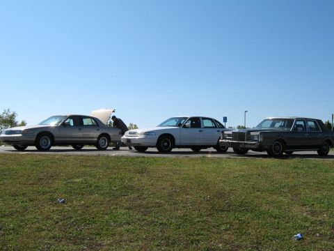 2000 Mercury Grand Marquis - Three sedans are parked on a grassy verge under a clear blue sky.