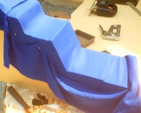 1999 Ford Taurus - A car part is covered in blue fabric, with tools like a jigsaw and stapler visible on a workbench.