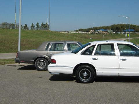 2000 Mercury Grand Marquis - Two sedans, one white and one gray, are parked outdoors on a sunny day.