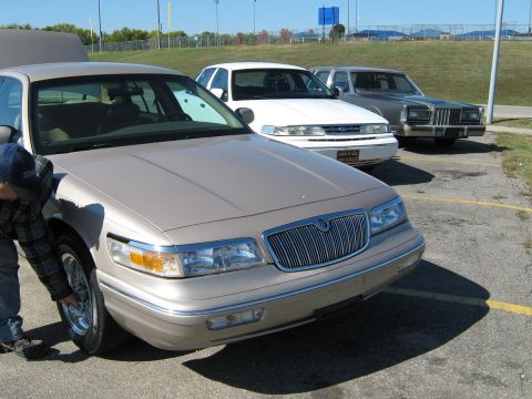 2000 Mercury Grand Marquis - A tan 2000 Mercury Grand Marquis is parked with its hood open, while a person inspects the front wheel.