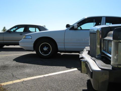 2000 Mercury Grand Marquis - A white sedan is parked next to a silver sedan, with a dark vehicle partially visible in the foreground.