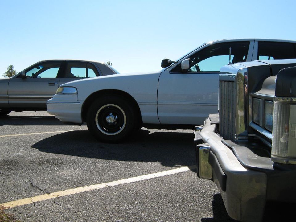 White sedan parked next to a silver sedan, with a dark vehicle in the foreground