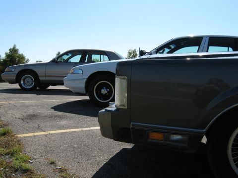 2000 Mercury Grand Marquis - Two sedans are parked on an asphalt lot with a yellow line marking a parking space.