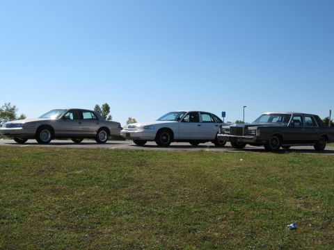 2000 Mercury Grand Marquis - Three sedans are parked on the side of the road on a sunny day.