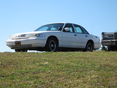 2000 Mercury Grand Marquis - White 2000 Mercury Grand Marquis seen from the front-right on a grassy incline with another vehicle nearby.