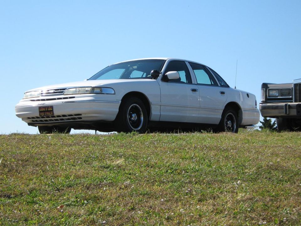 White 2000 Mercury Grand Marquis parked on a grassy hill, another vehicle partially visible to the right