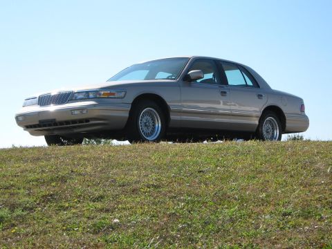 2000 Mercury Grand Marquis - This 2000 Mercury Grand Marquis is seen from a three-quarter front view, parked on a grassy incline under a clear blue sky.