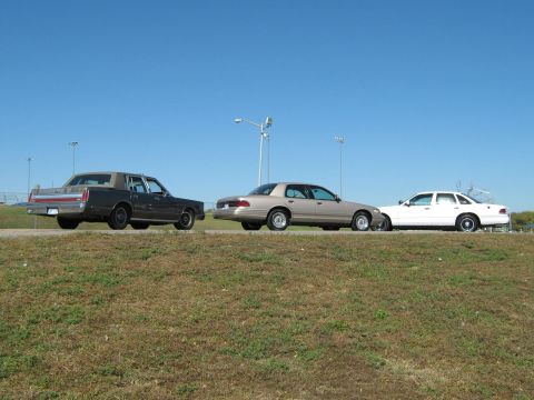 2000 Mercury Grand Marquis - Three sedans are parked side-by-side on a grassy embankment with a clear blue sky overhead.