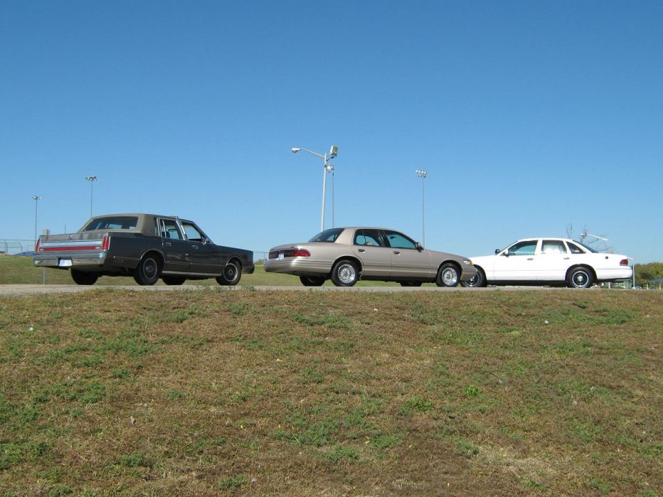 three sedans parked on a grassy incline under a clear blue sky