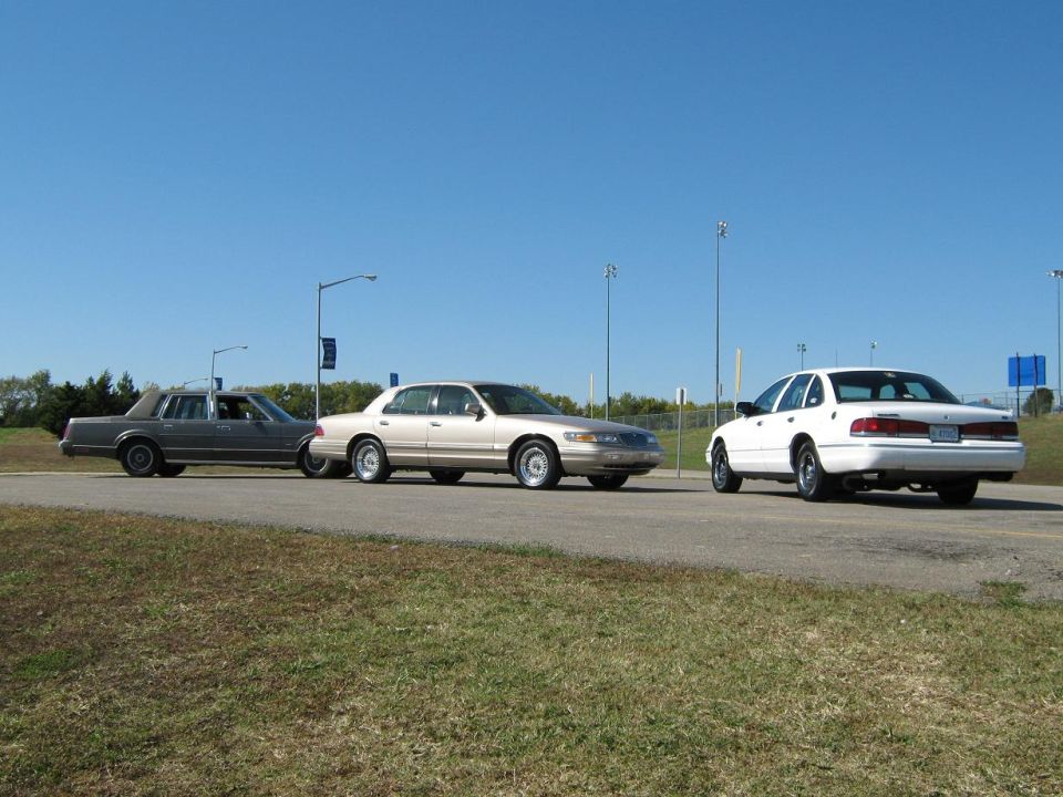 Three sedans, including a white 2000 Mercury Grand Marquis, parked on a road