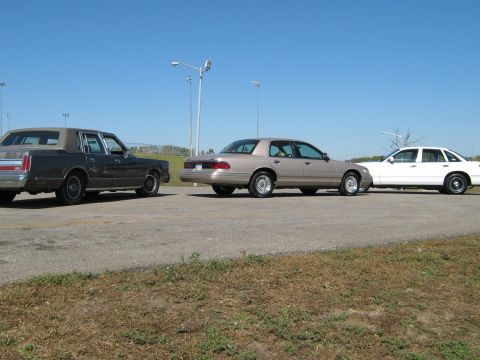 2000 Mercury Grand Marquis - Three sedans, including a 2000 Mercury Grand Marquis, are parked side-by-side on an asphalt surface.