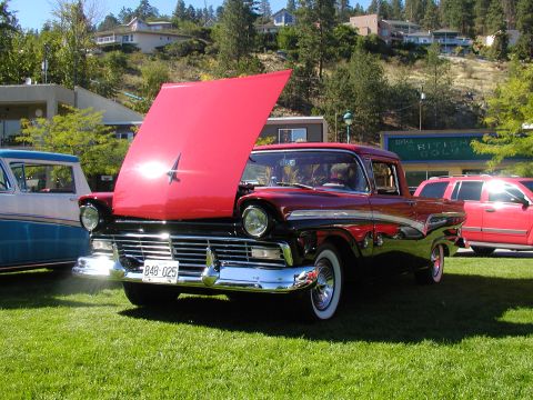 1967 Ford Ranchero - A two-tone red and black 1957 Ford Ranchero is displayed with its hood open, parked on a grassy field next to other vehicles.