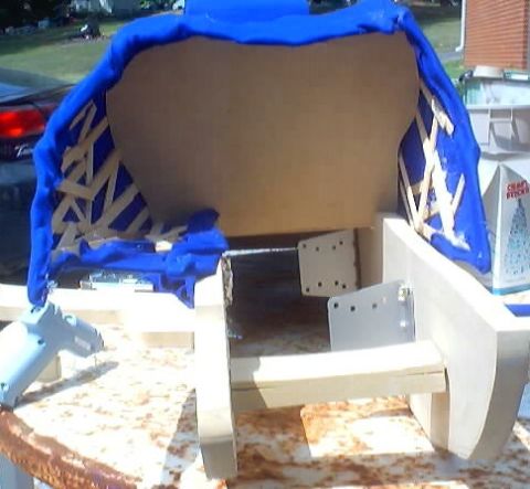 1999 Ford Taurus - A car seat frame, partially covered in blue fabric and reinforced with wooden supports, is undergoing work, with a hot glue gun visible on…