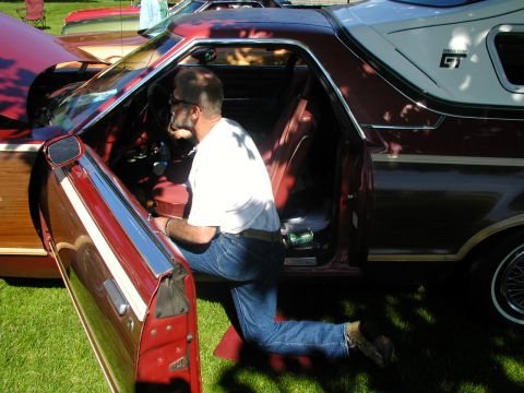 1967 Ford Ranchero - A man kneels in the driver's seat of a maroon and woodgrain Ford Ranchero, with the door open.