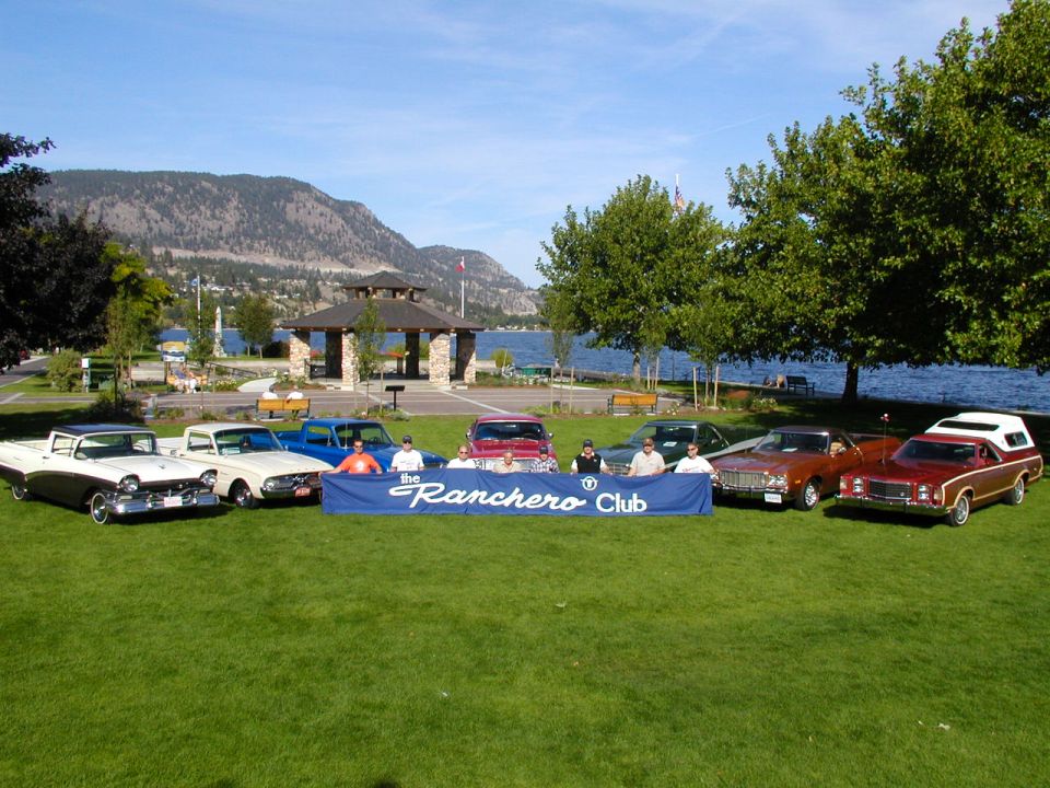 Eight Ford Rancheros lined up on lakeside lawn behind a navy Ranchero Club banner