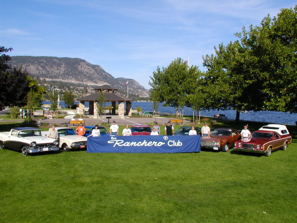 Row of Ford Rancheros and owners behind a Ranchero Club banner by a lake